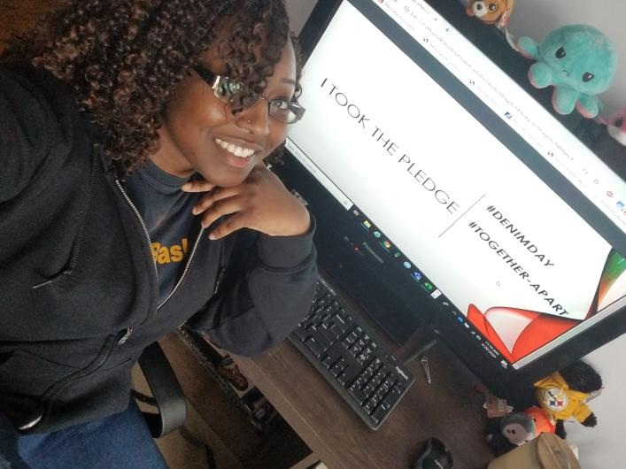 Andrea Shorter from OCR sitting next to her computer, reads on screen: I took the Pledge #DenimDay sign.