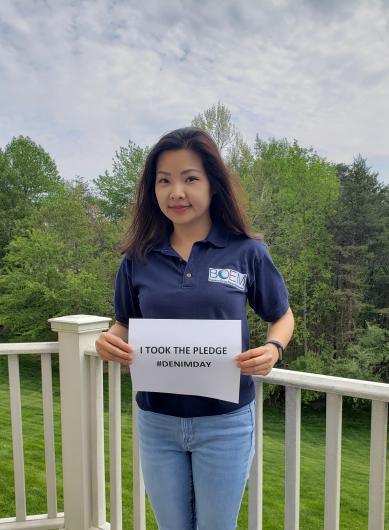 Annie Yang from BOEM, outside on a deck holding the I took the Pledge #DenimDay sign. 