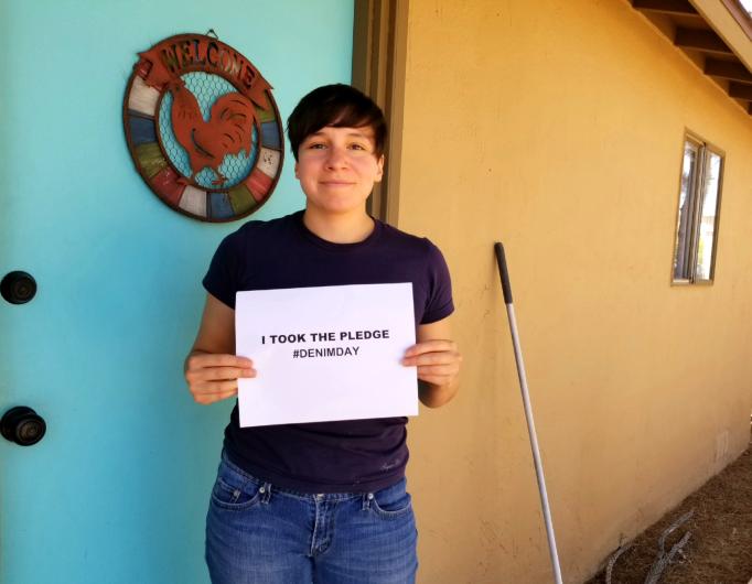 Brenna Rodriguez from NPS, standing outside holding the I took the Pledge #DenimDay sign.