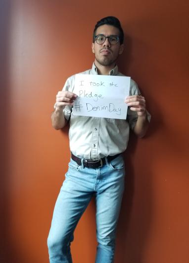 Sean Binninger from FWS standing in front of red wall, holding the I took the Pledge #DenimDay sign. 