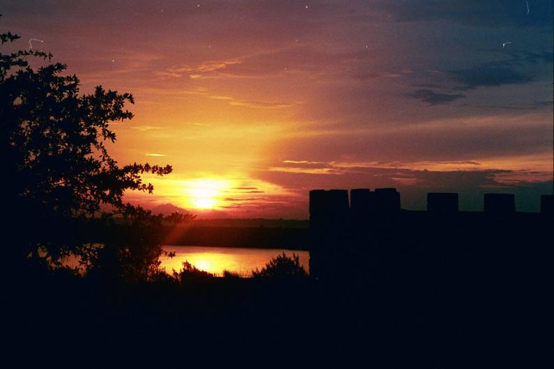 The sun rises above the ruins of an old fort next to marsh.
