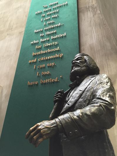 A statue of Frederick Douglass standing next to a sign in a visitor center.