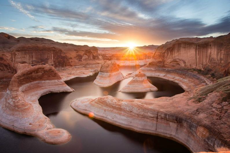 The sun shines down on a twisting canyon filled with dark water.