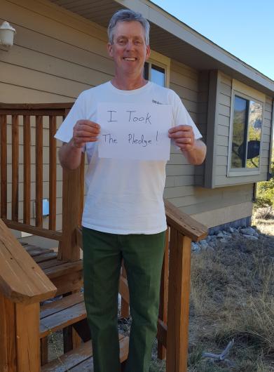 John White from NPS standing outside a house holding the I took the Pledge #DenimDay sign.