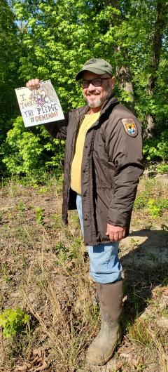 Leo Miranda from USFWS, outdoors holding an I took the Pledge #DenimDay sign hand written with drawing. 