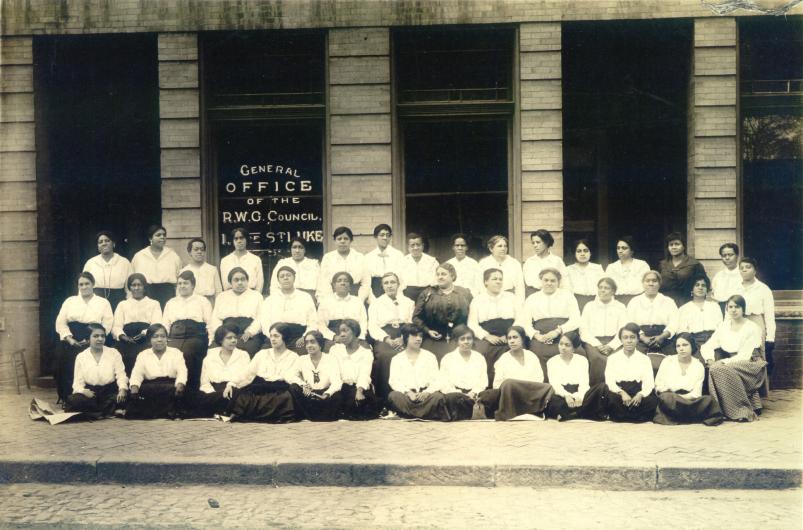 Maggie L. Walker posing with other women in the the Independent Order of St. Luke. Photo in the Public Domain. A historic black and white photo of a group of about 50 African American women posing in front of a brick building with large windows.