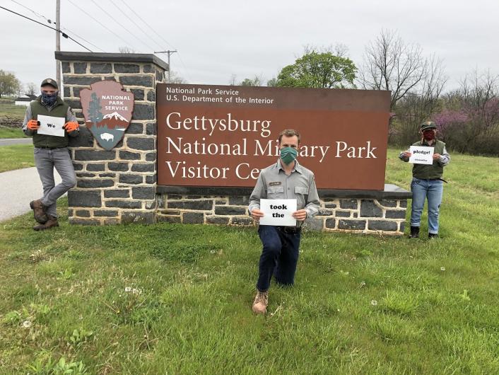 Three men by the Gettysburg National Military Park's entrance, each holding one side: We; Took The; Pledge #DenimDay. 