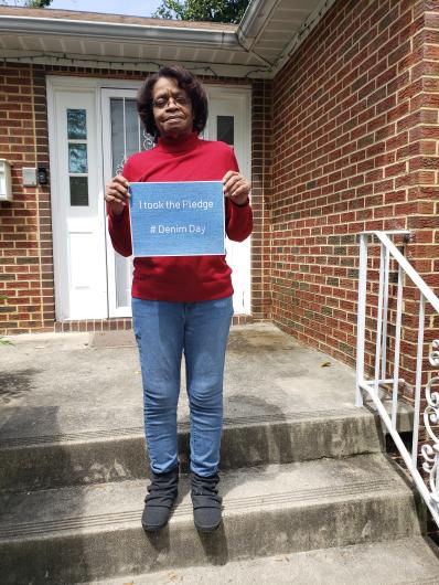 Patricia Callis from BSEE, outside a house's entrance holding the I took the Pledge #DenimDay sign.