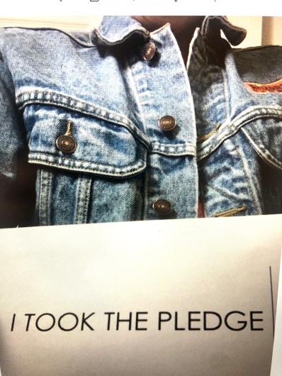 Sandra Etos from USBR on a close up shoot, no face showing, wearing a denim jacket holding the I took the Pledge #DenimDay sign.