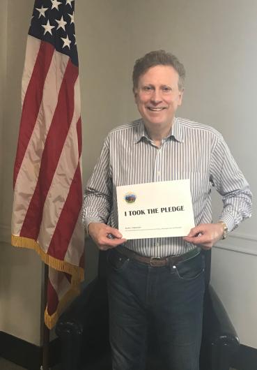 Scoot Cameron from 0S-PMB holding the I took the Pledge #DenimDay sign. At his back, the American flag. 