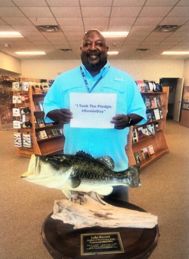 Earl (Tank) Gibson from NPS standing next to fish trophy, holding the I took the Pledge #DenimDay sign.