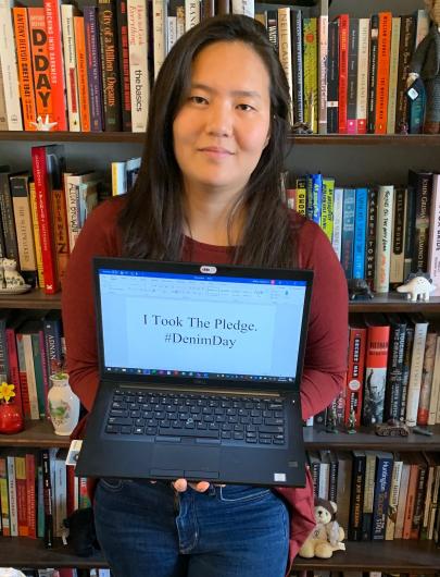 Katherine Willard from NPS standing in front a bookcase, holding the I took the Pledge #DenimDay sign.