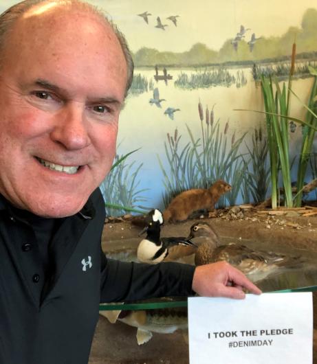 Charles Wooley from USFWS holding the I took the Pledge #DenimDay sign. At his back, wildlife set up exhibit item