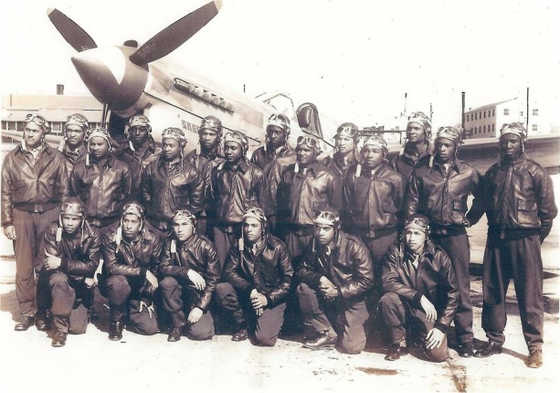 Tuskegee Airmen graduates from advanced single-engine pilot training pose in two lines in front of a World War 2 fighter plane.