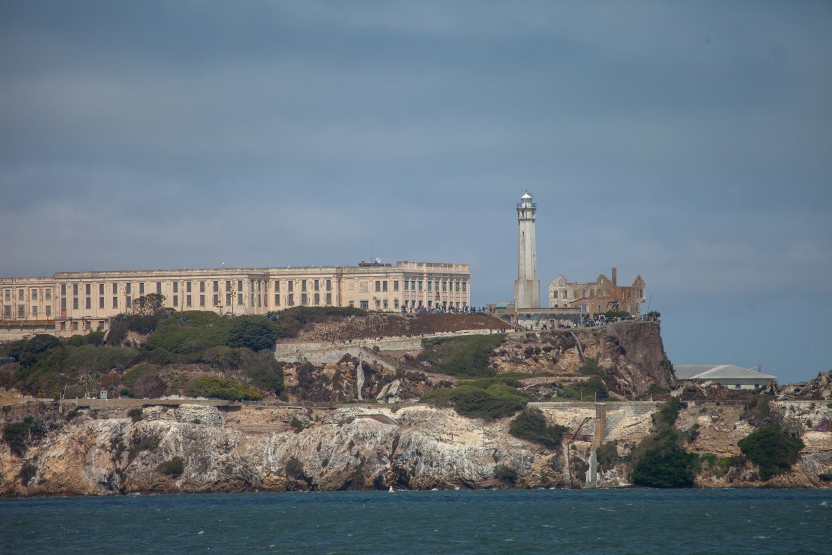 A large white building sits on a island surrounded by water. A tower stands on top of the rocky terrain.