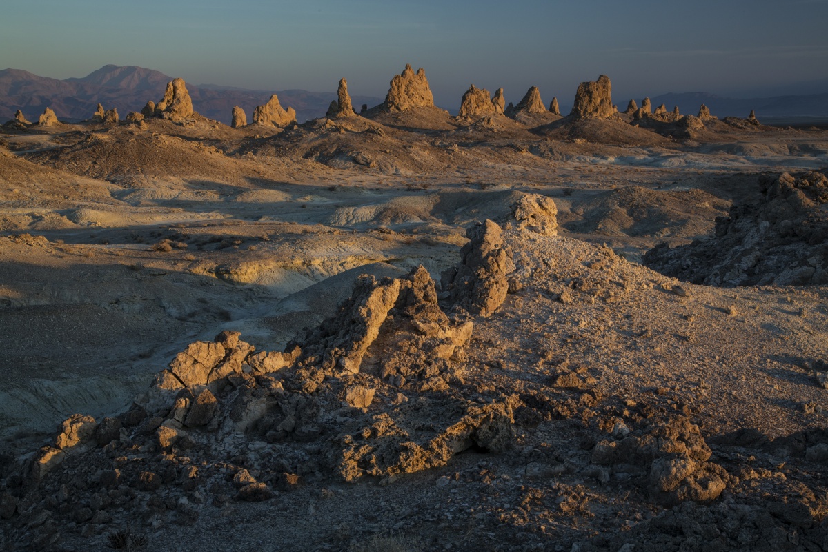 The sunset casts a warm yellow glow on rocky pinnacles against a light blue sky