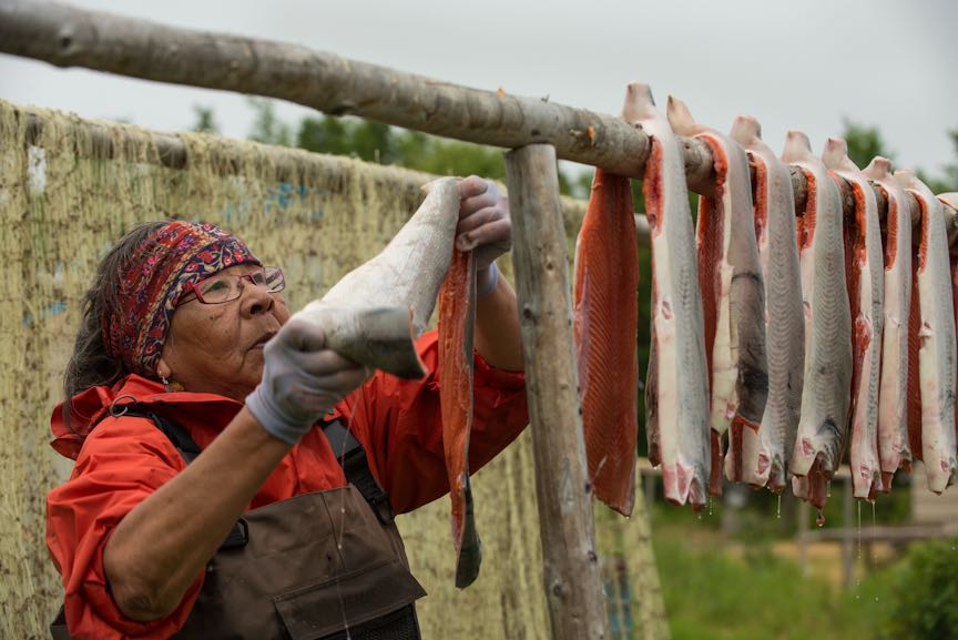A woman wearing bright orange hangs fish on a wooden drying rack.