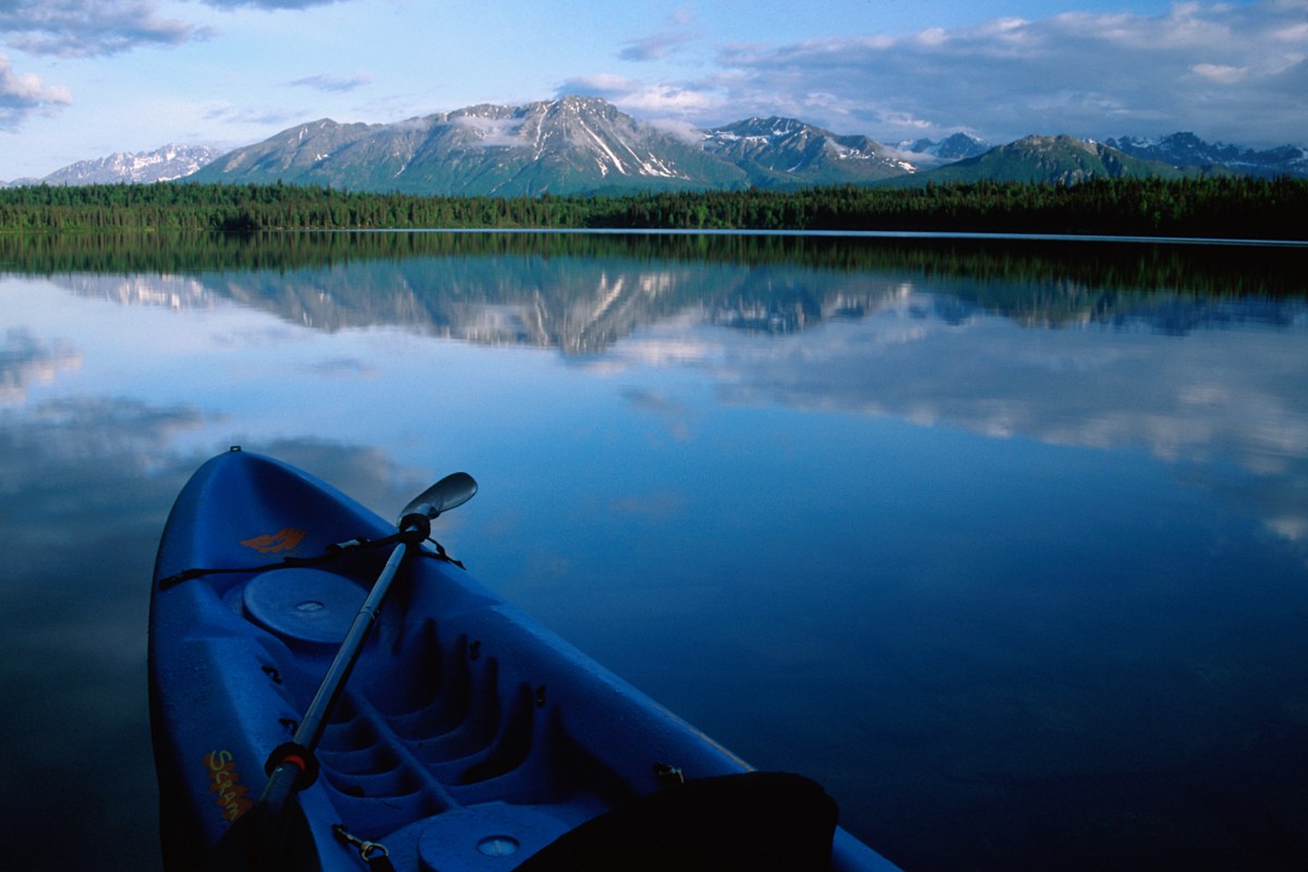 Blue kayak on Delta Wild and Scenic River in Alaska with forest and mountain in the background.
