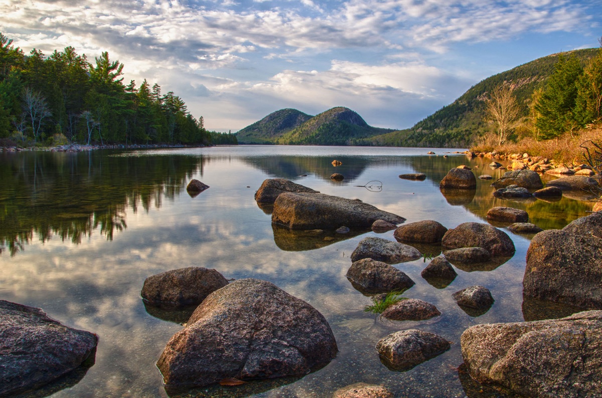 pond with rocks in the foreground surrounded by green hills and blue sky