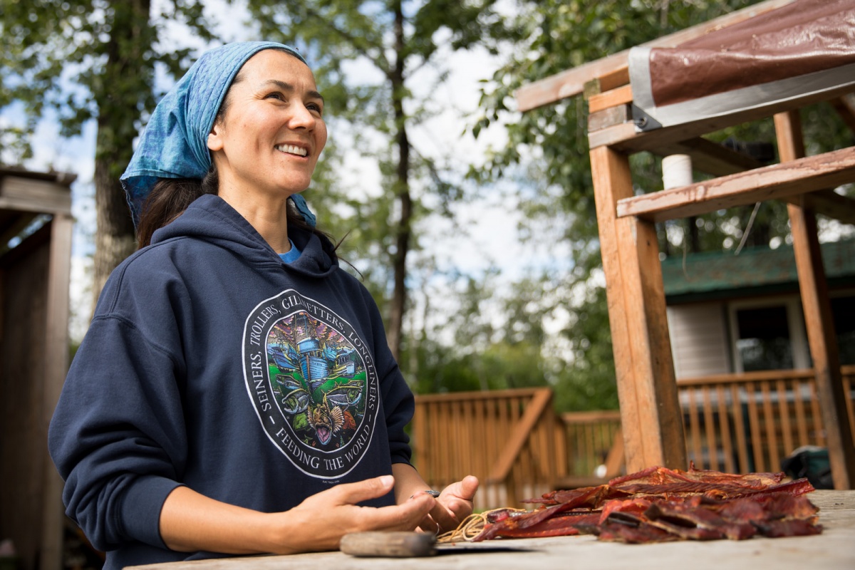 A smiling woman stands at an outdoor table with dried fish on it.
