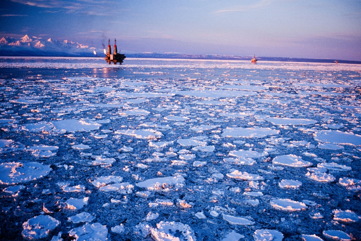 An drilling platform stands above the still water of an ice covered ocean.