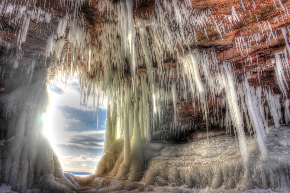 Large icicles hang from the ceiling of a large rock cave.