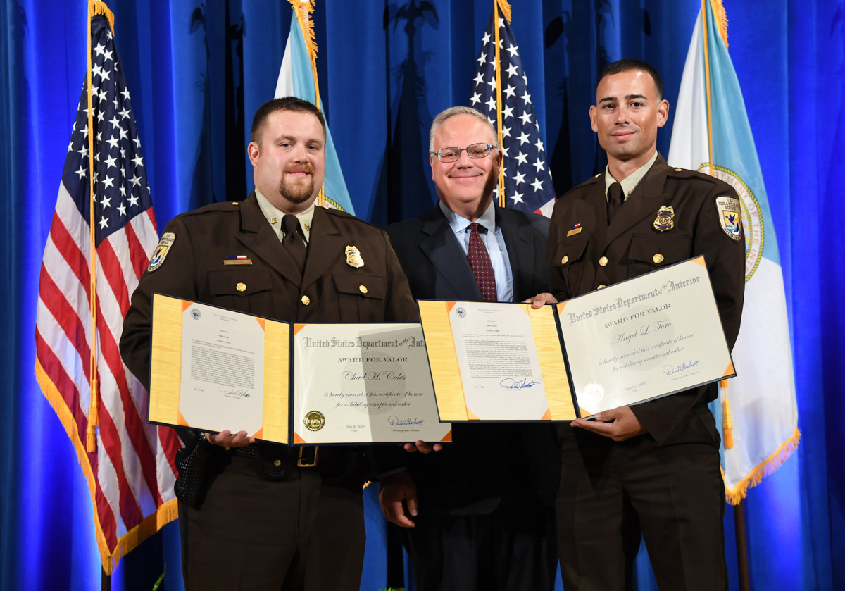 Two men in Fish and Wildlife Service uniforms stand next to a man in a suit and hold certificates.