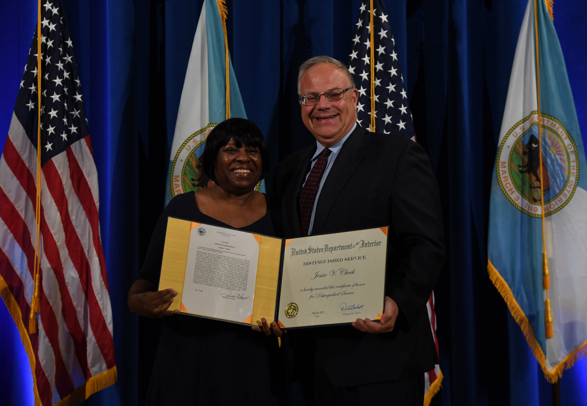 An African American woman and a white man in a suit pose together holding a certificate.