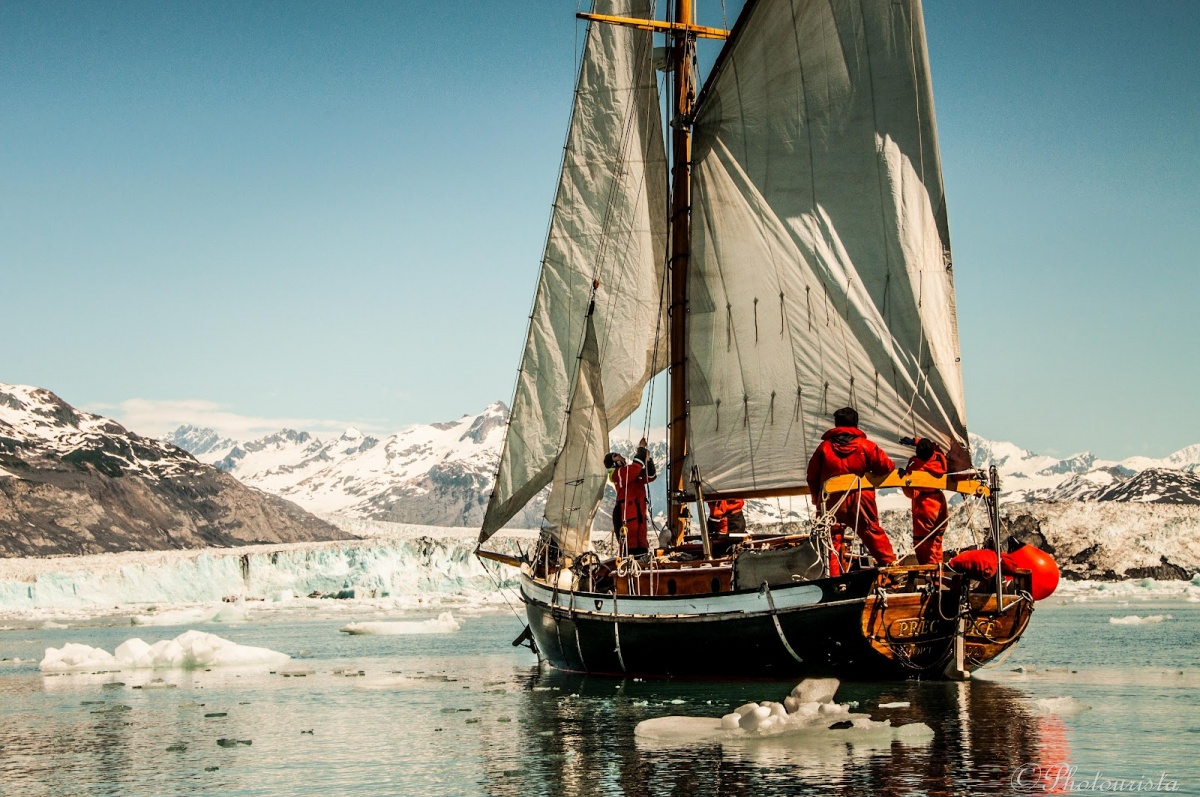 Three people on a sailboat bringing it to shore in Nome, Alaska