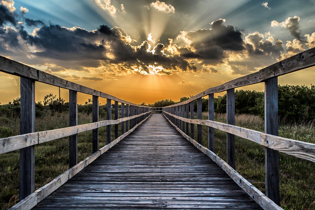 sunlight bursting through clouds over a walkway