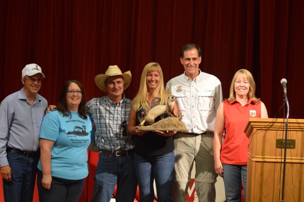 Four members of the Hogg family stand on a stage with U.S. Fish and Wildlife officials while holding a stuffed black footed ferret.
