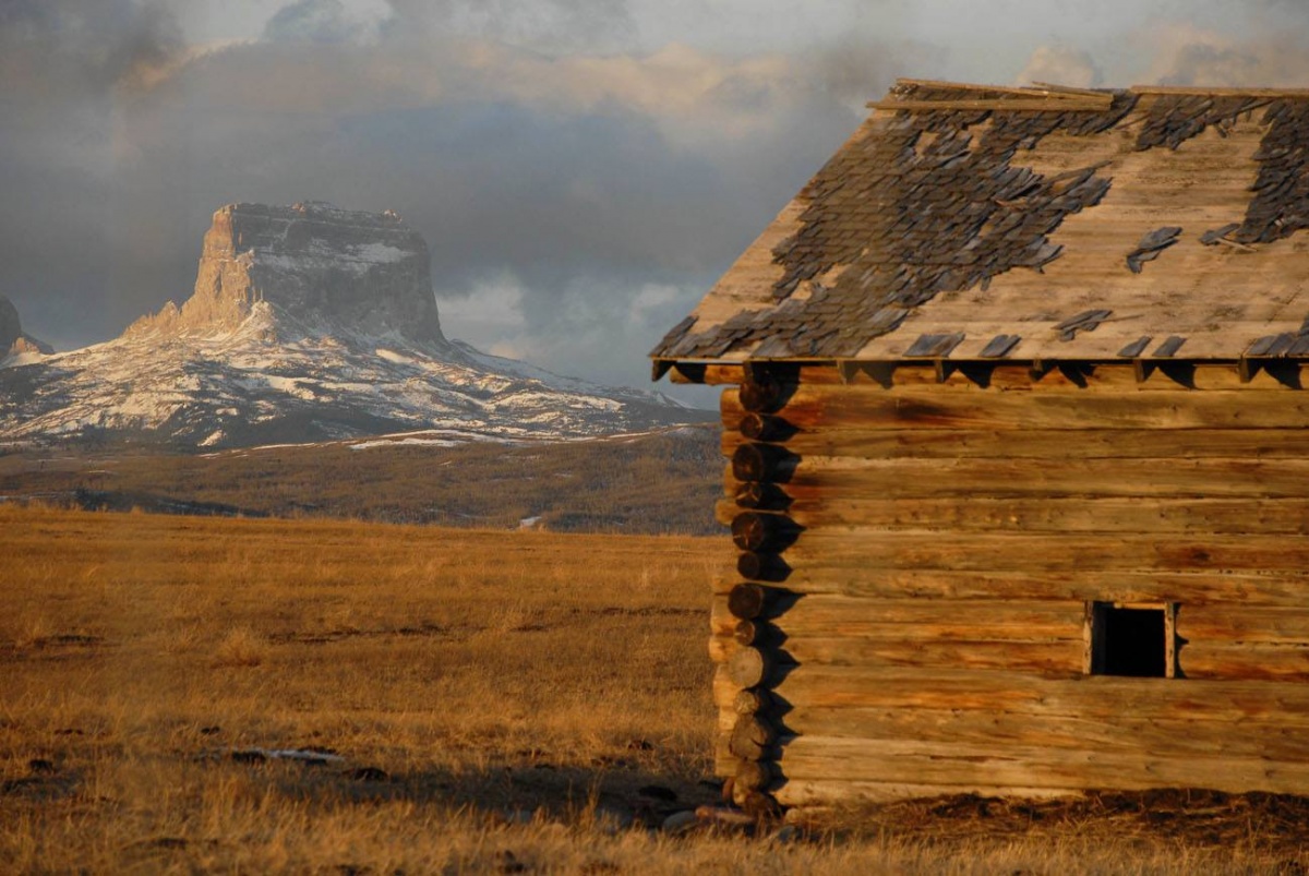 A wooden hut occupies the foreground of the picture while a mountain structure sits in the background. 