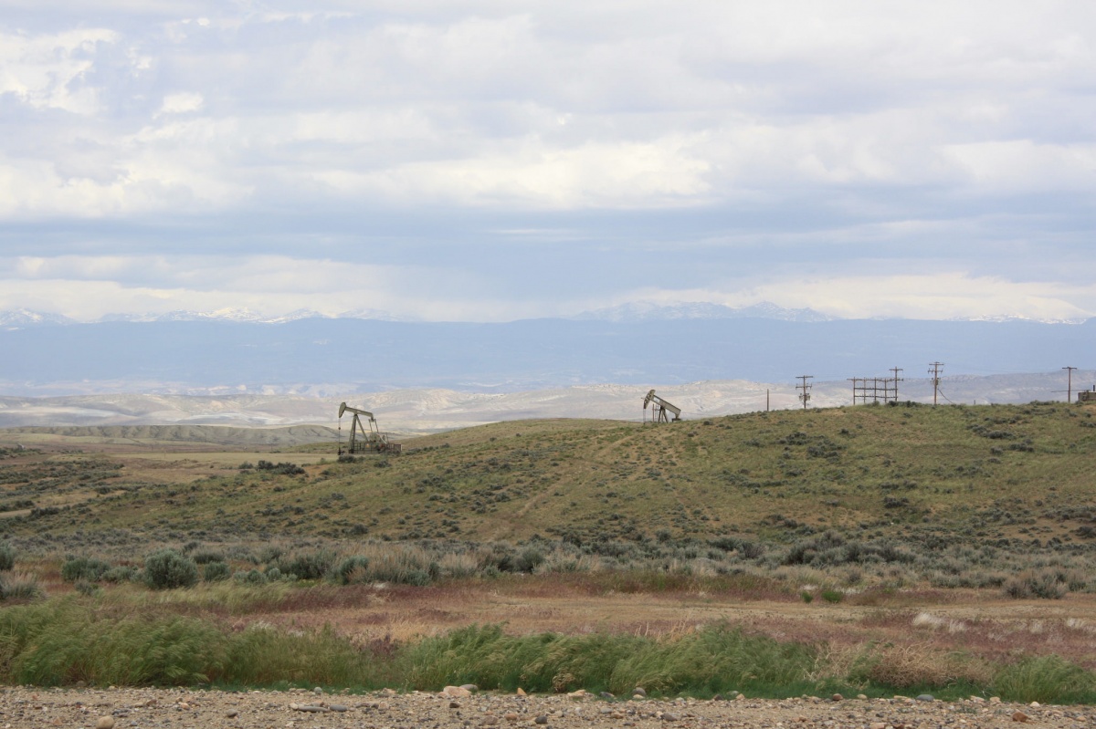 Two oil pumpers dot rolling hills with mountains looming in the distance.