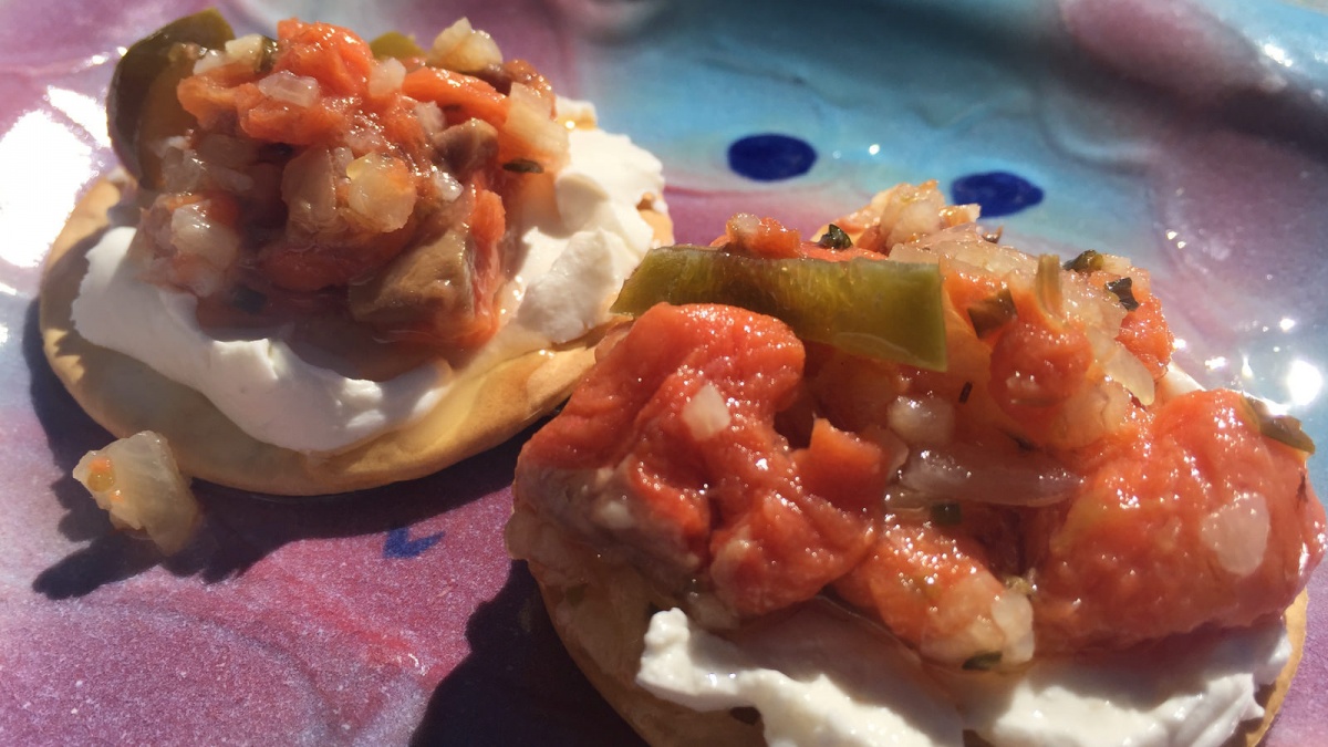 Orange salmon mixture sits atop two crackers on a blue and pink plate.