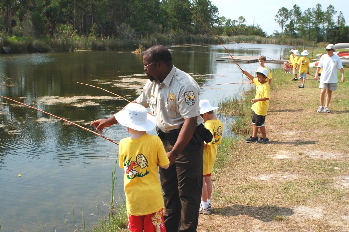 Ranger Bruce Butler teaches Cub Scouts in yellow shirts to fish in Brunswick, GA.