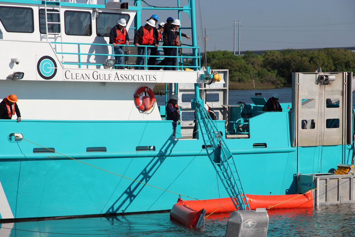 A crew on a large metal boat drop long sections of inflated booms on to the water.