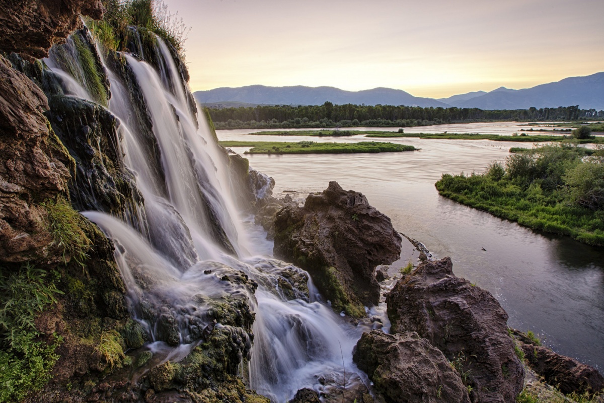 A waterfall flows into a river as the sunsets