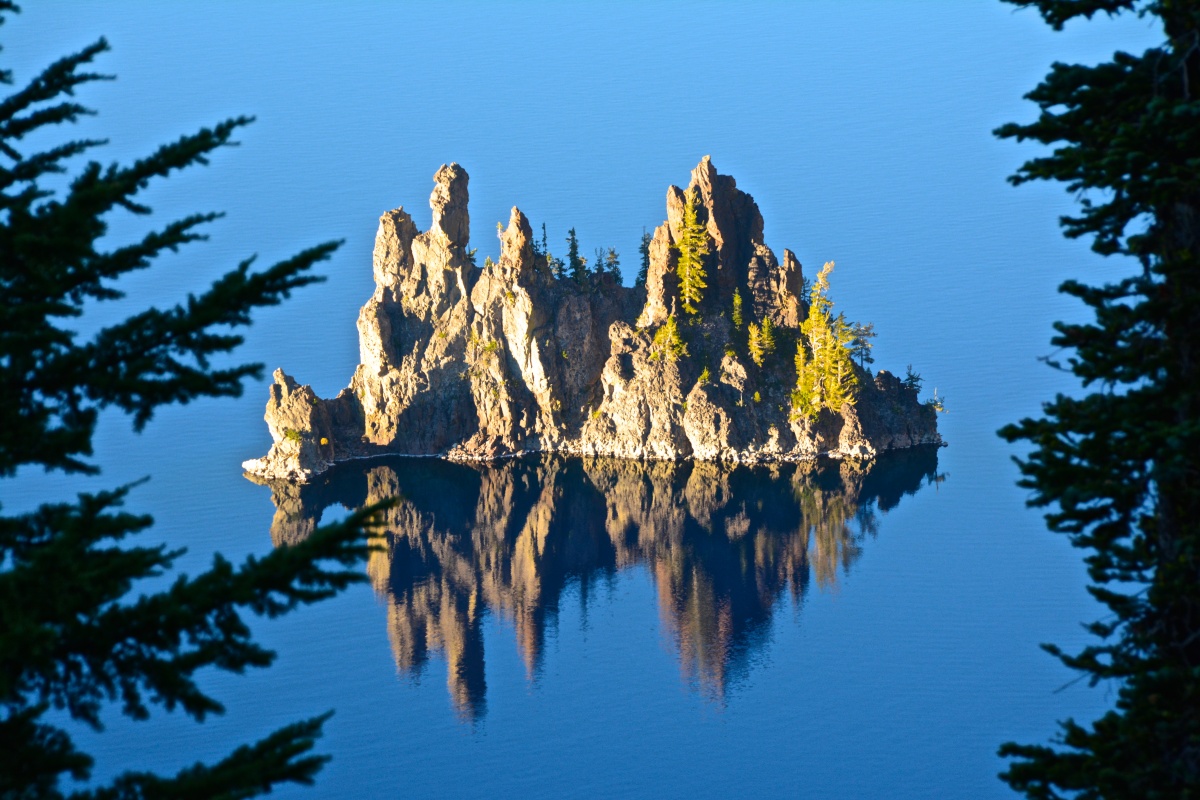 Una pequeña isla con altas torres de roca y algunos árboles se levanta de las tranquilas aguas de un lago.