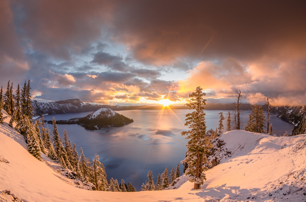 L'alba raggiunge il picco sul labbro di una cresta innevata che circonda un lago di montagna circolare.