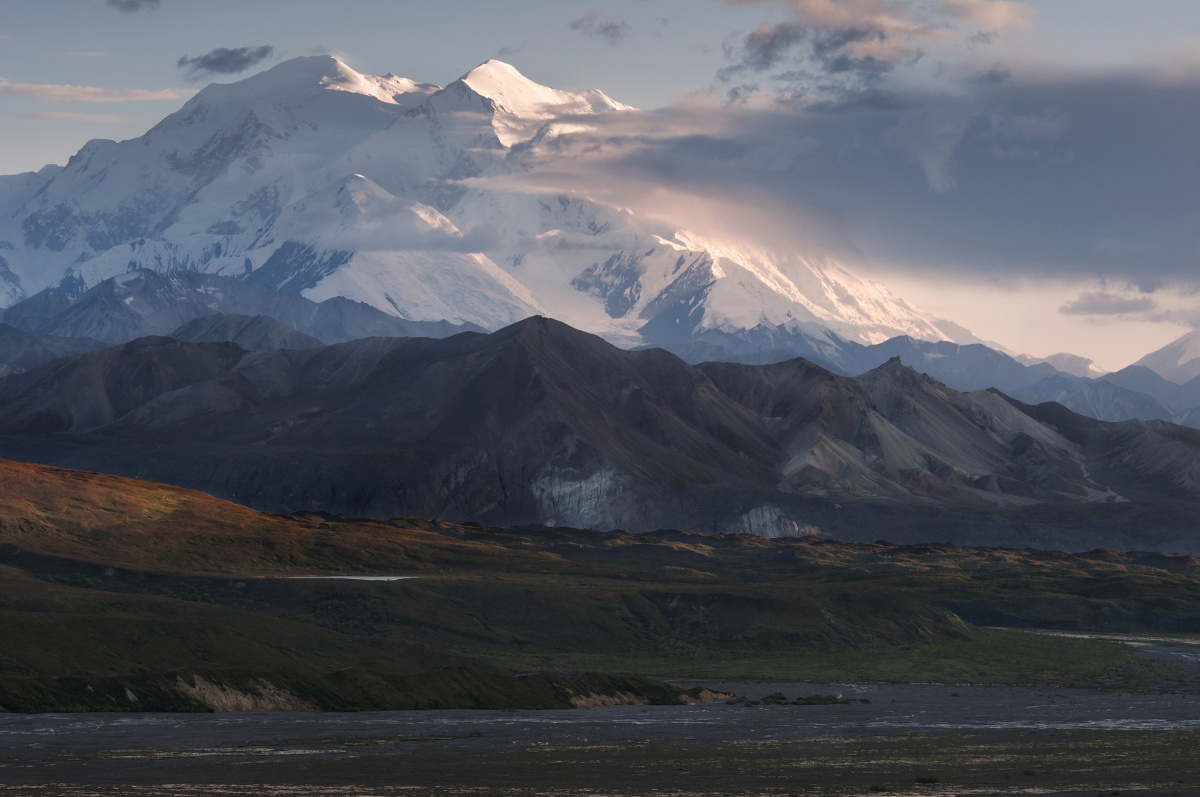 A massive snow covered mountain rises about low brown foothills.