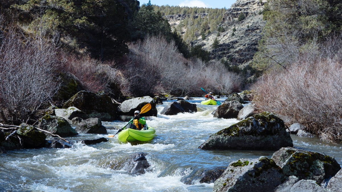 Paddlers navigate their bright green rafts through whitewater rapids and rocks in Oregon's Donner und Blitzen Wild and Scenic River.