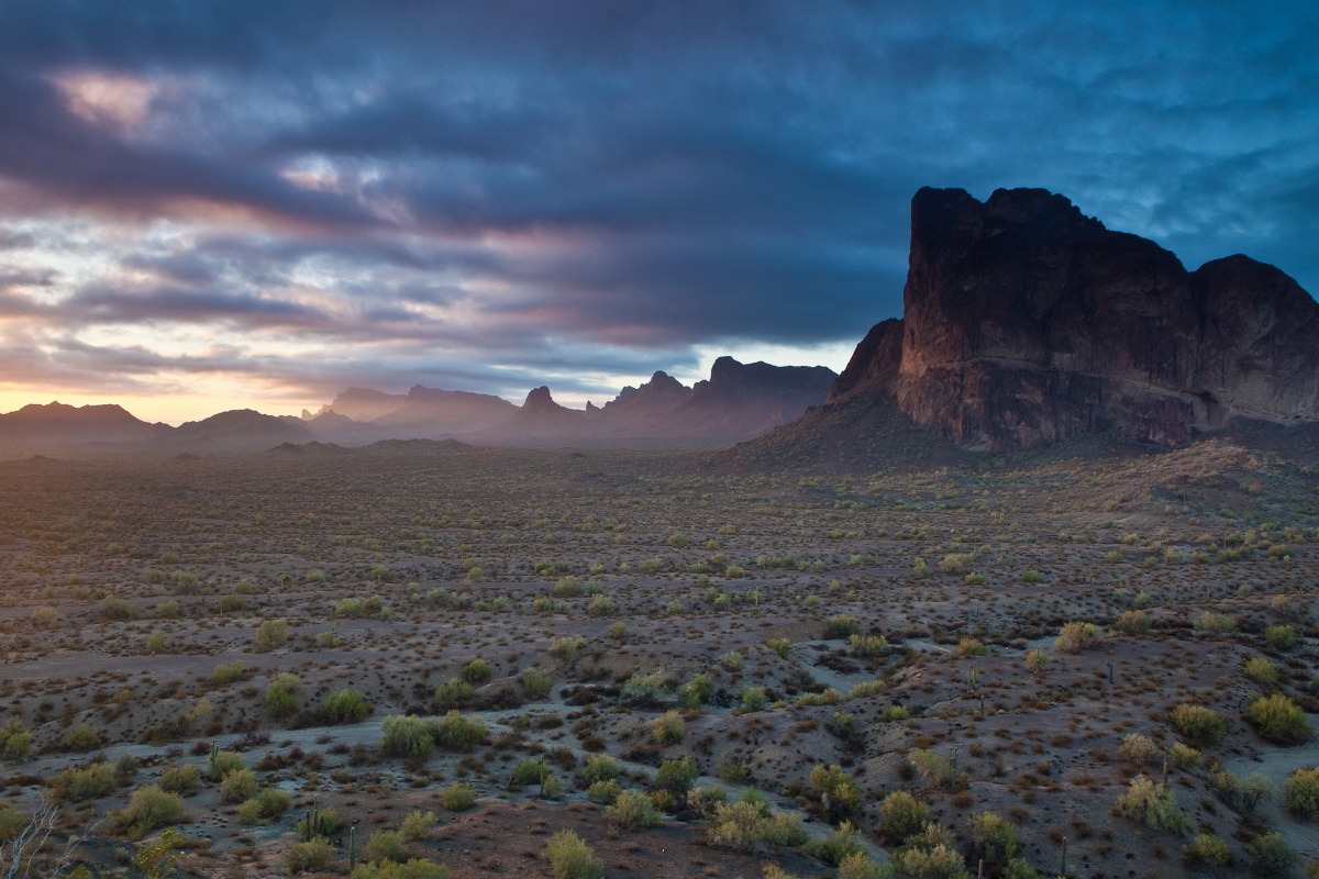 A dark stormy sky looms in the background as Eagle Tail Mountain juts up from a desert floor.