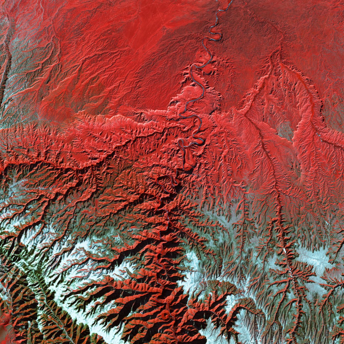 A satellite photo looking down on a red landscape of a mountain range spreading out in jagged lines.