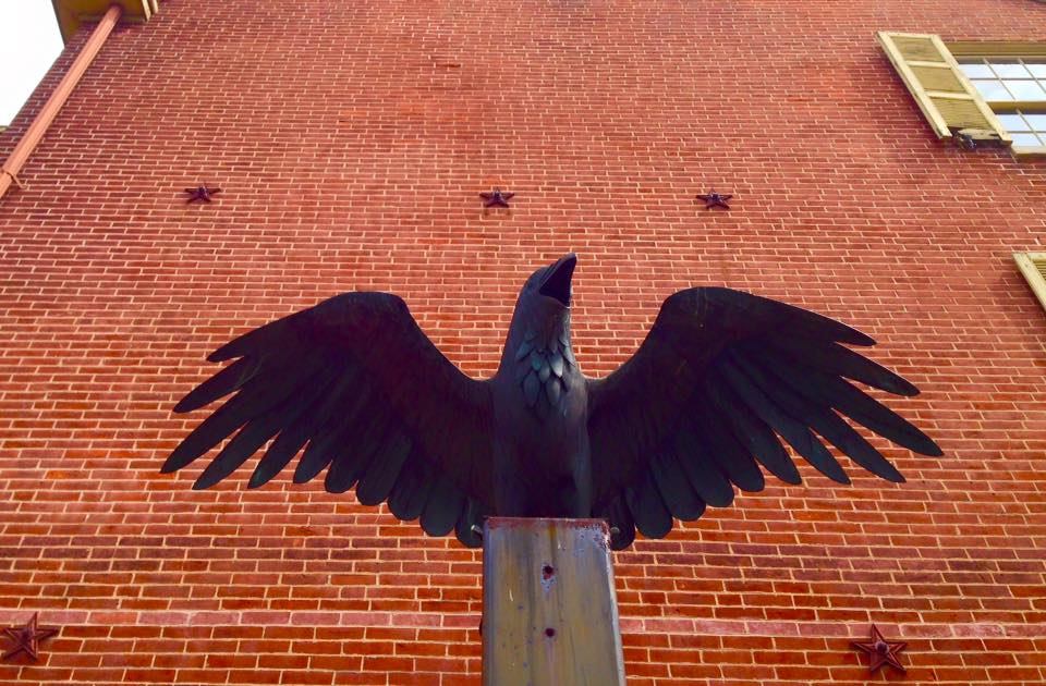 A metallic raven statue stands intimidating with its mouth open wide in front of Edgar Allan Poe's colonial-style old brick home.