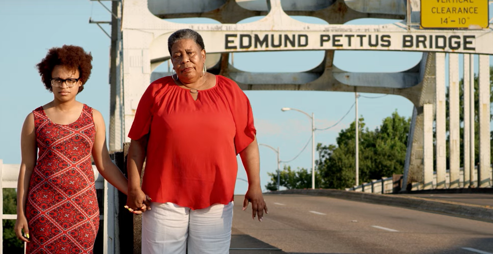 Two women stand hand in hand at the Edmund Pettus Bridge