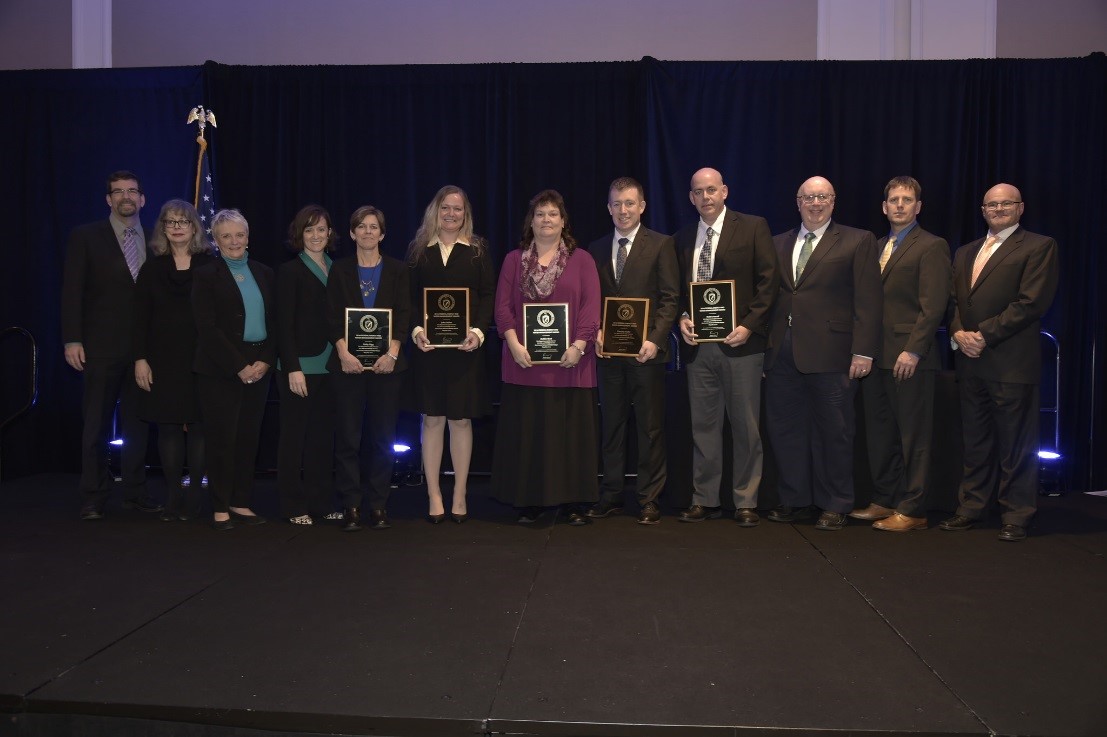 A group of men and women holding plaques stand in a line.