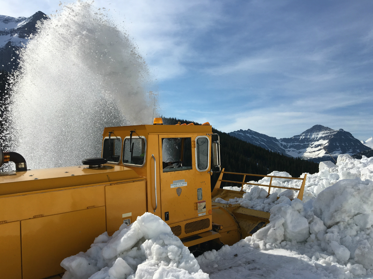 A big yellow snow blower, clearing a snow covered road.