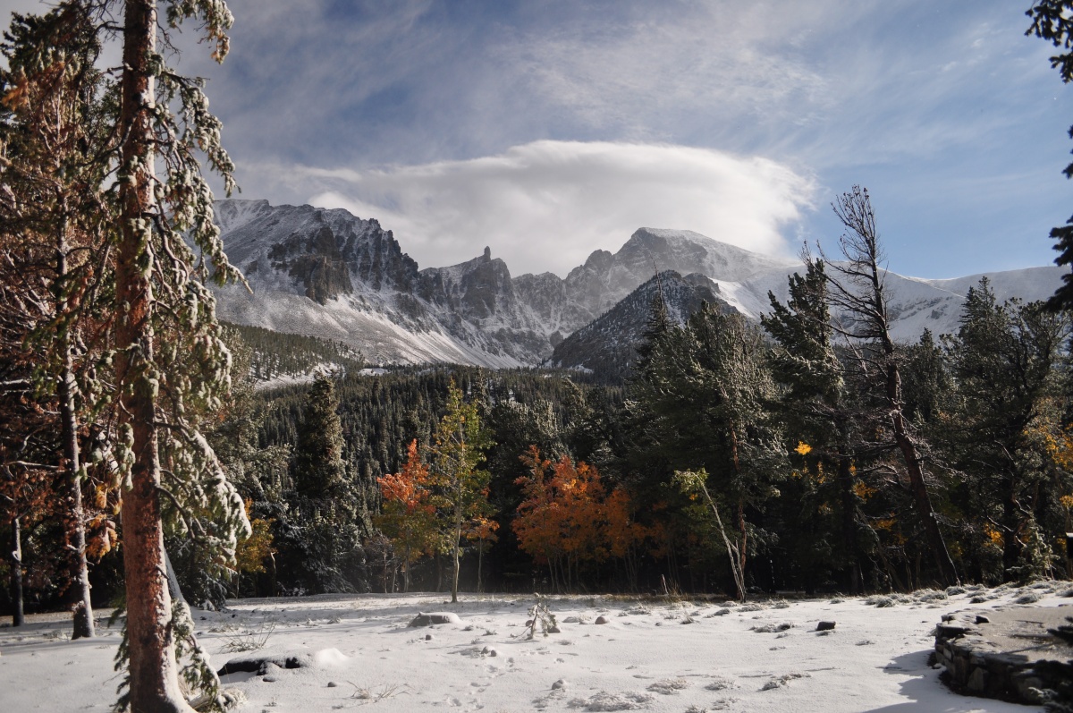 A long mountain slopes down to hills and a flat meadow covered in snow.