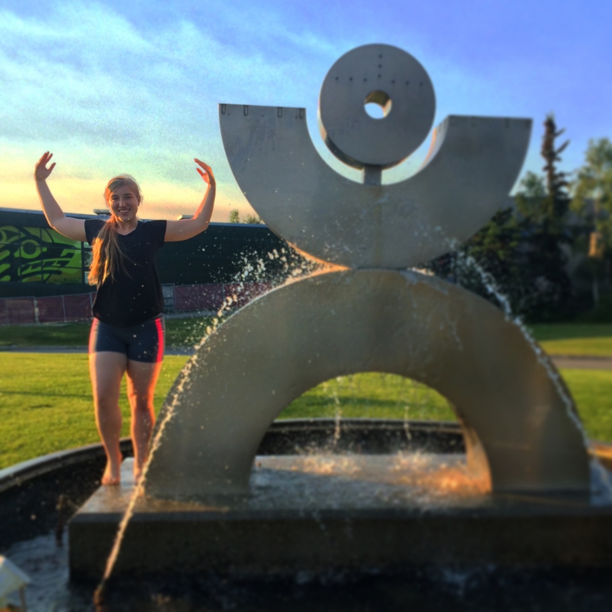 Girl stands with arms stretched in front of waterfall