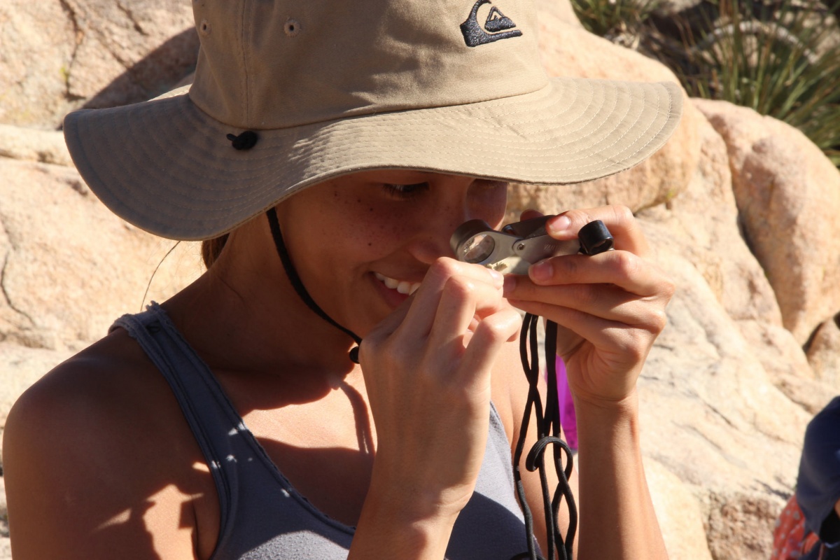 A volunteer wearing a safari hat looks into a microscope while examining a plant.